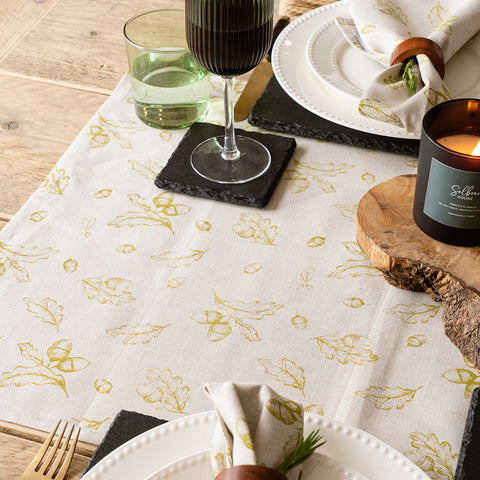 Cream-colored linen table runner with gold leaf and acorn pattern and subtle textured weave for autumn decor