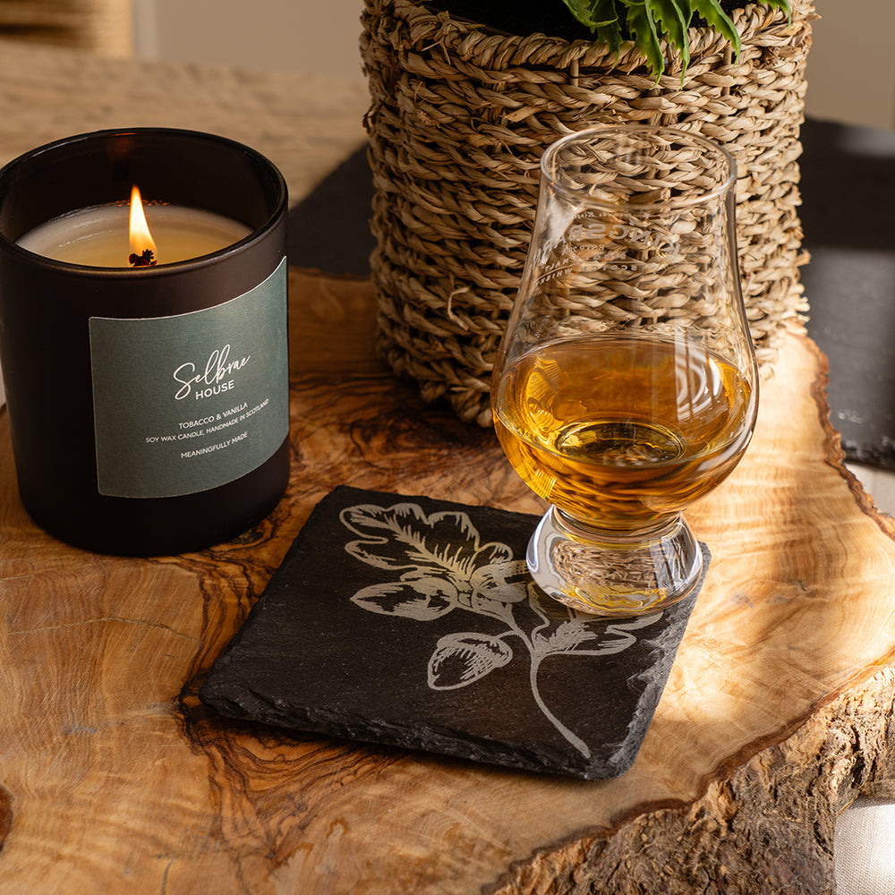 Black cylindrical candle with lit wick and green selfie house label on autumn acorns single slate coaster