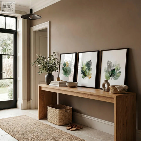Three prints of autumn art botanical leaf watercolor green and gold tone leaves in black frames on a brown wall