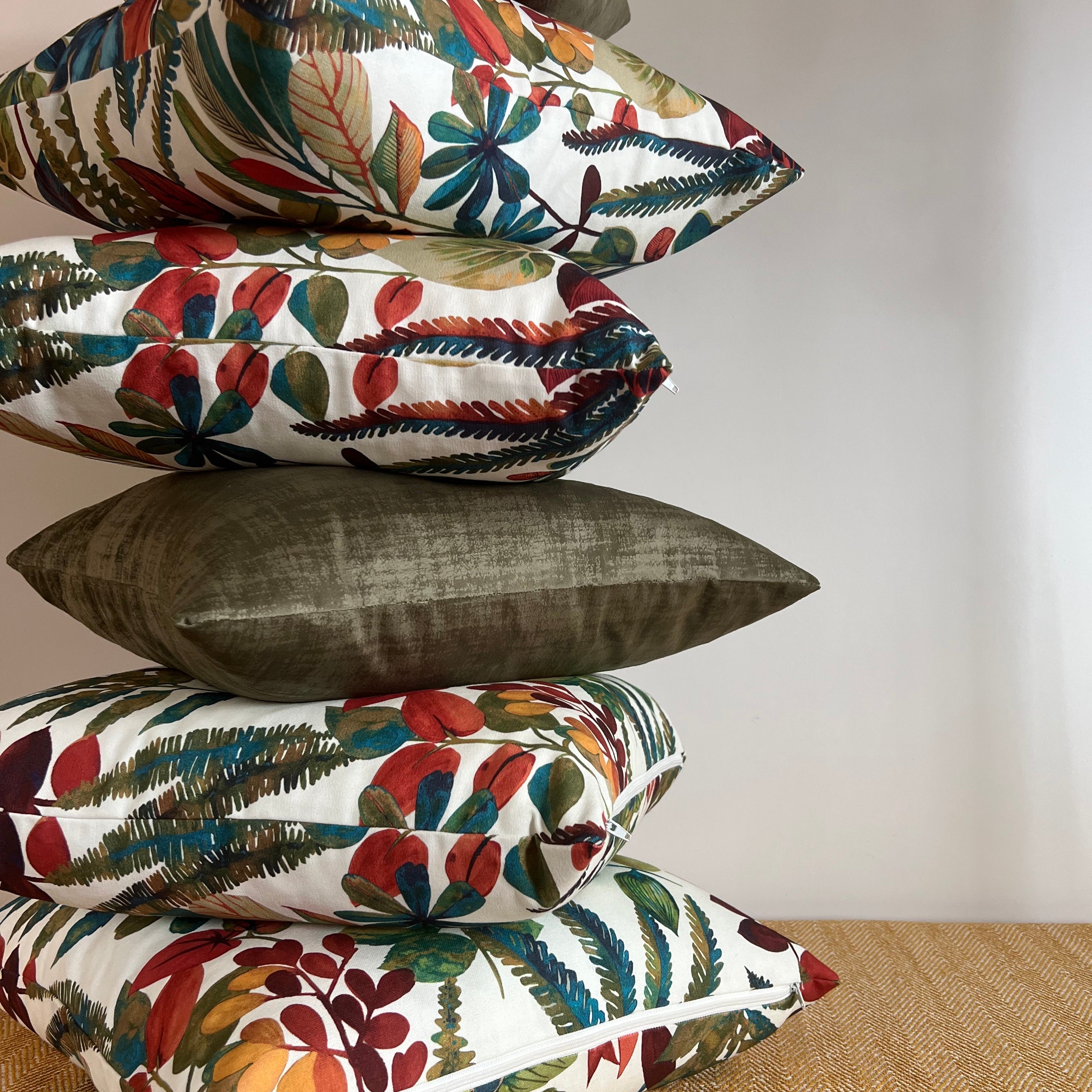 Stack of autumn leaves cotton throw cushions with vibrant botanical prints and an olive green velvet pillow
