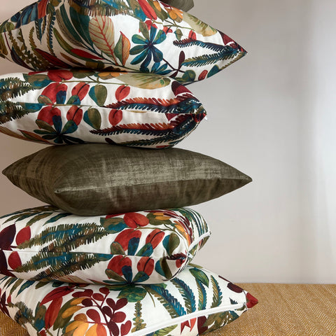 Stack of autumn leaves cotton throw cushions with vibrant botanical prints and an olive green velvet pillow