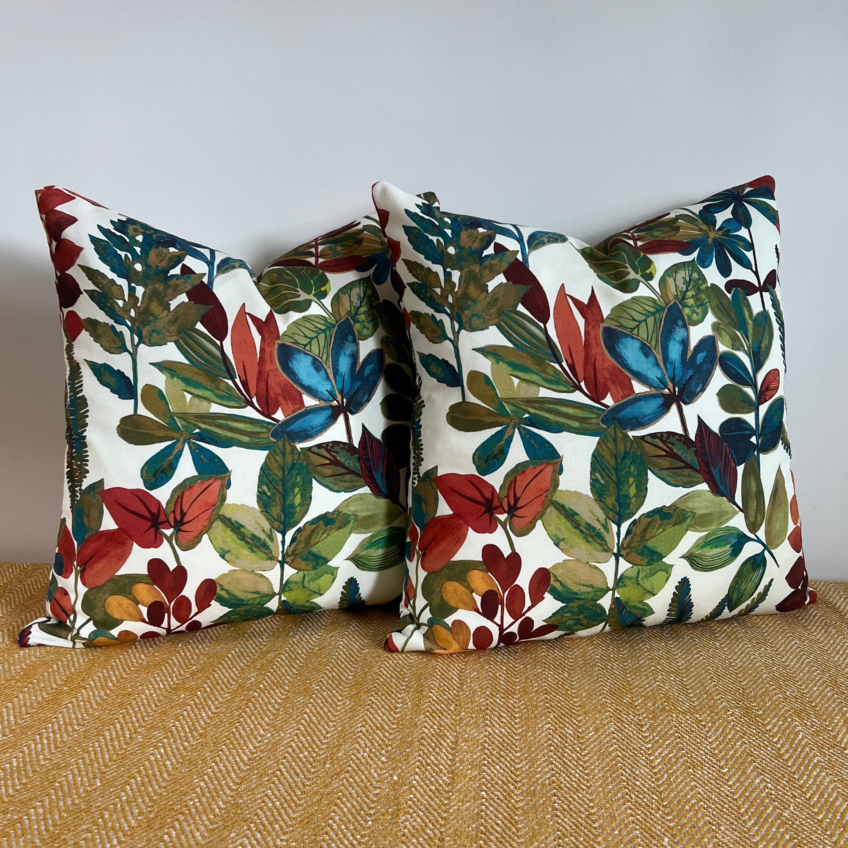 Two square cotton throw cushions with vibrant red blue and green autumn leaves cotton print on off white background