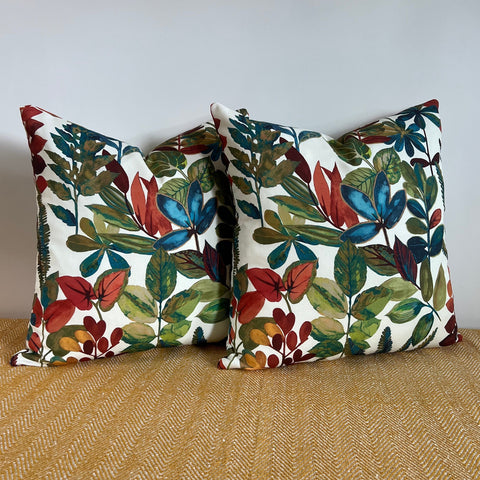 Two square cotton throw cushions with vibrant red blue and green autumn leaves cotton print on off white background