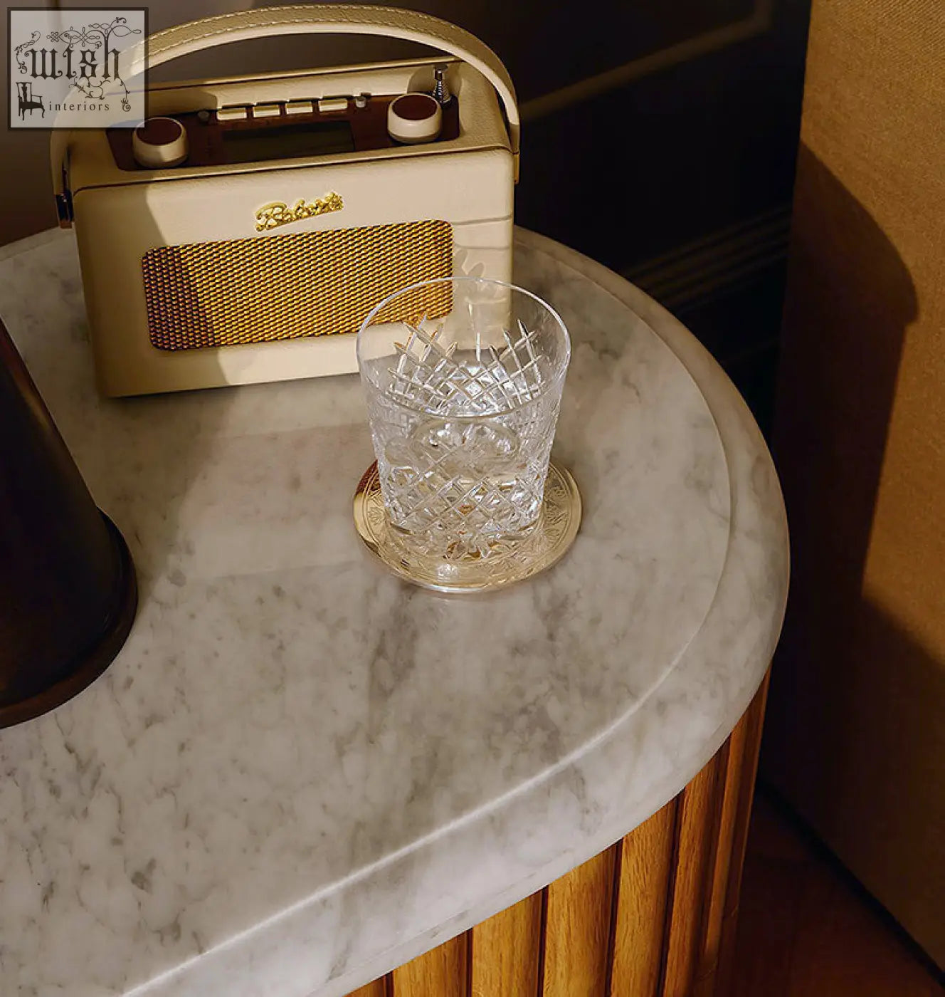 Cream-colored bakelite radio with gold mesh grille and dials on marble rounded rectangle bedside table