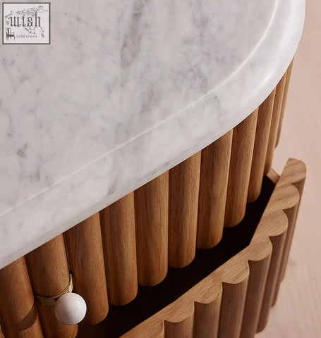 A sleek white marble rounded rectangle bedside table top with curved edge supported by honey-toned wooden slats