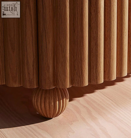 A warm-toned wooden rounded rectangle bedside table with vertical fluted panels and a ribbed spherical foot