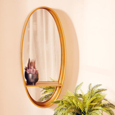 Avento gold oval wall mirror with gold oval frame and wooden shelf holding pink and green succulent pot