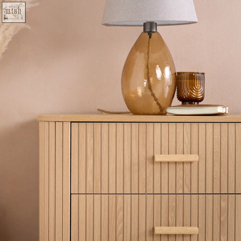A sleek amber glass table lamp with a textured gray fabric shade and braided cord detail in the fluted bedroom range