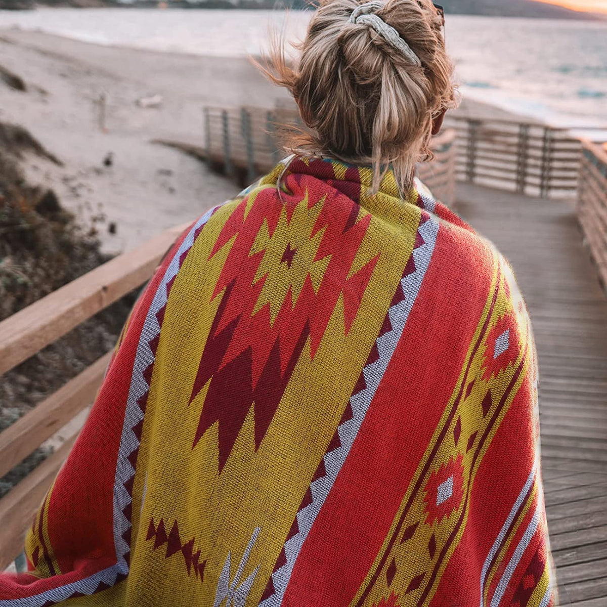 A vibrant red and yellow aztec pattern throw blanket with soft sherpa lining draped over a person’s shoulders