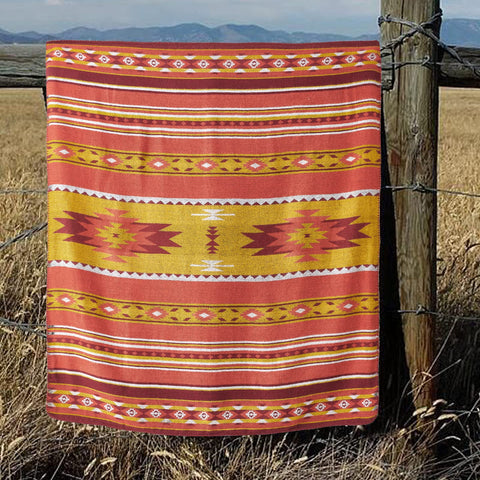 A vibrant red and yellow aztec pattern throw blanket with soft sherpa lining hanging on a rustic fence
