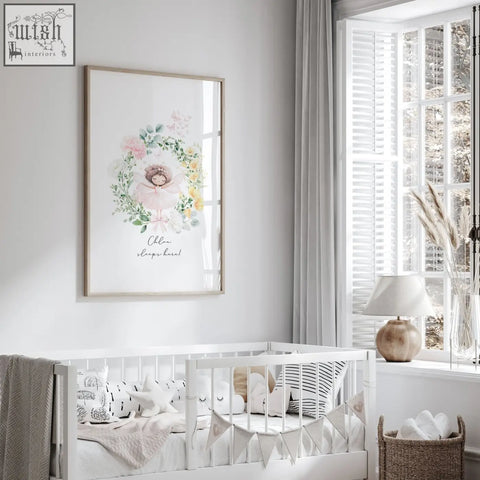 A framed watercolor wall art print of a sleeping baby in a pink and green floral wreath perfect for a baby’s room