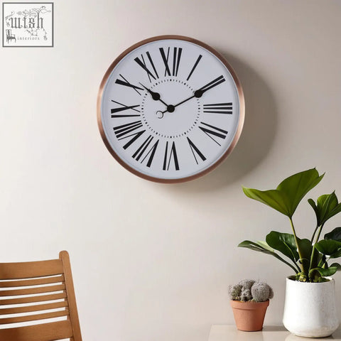 Baillie rose gold wall clock with a copper-toned frame white face and black roman numerals rose gold wall decor