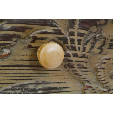 A bali coffee table with a round light beige wooden drawer knob on a dark intricately carved surface
