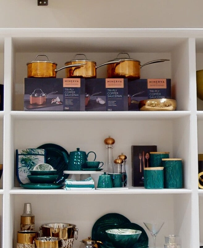 Set of three minerva tri-ply copper saucepans displayed next to a bali dark green storage jar with bamboo lid on white shelf