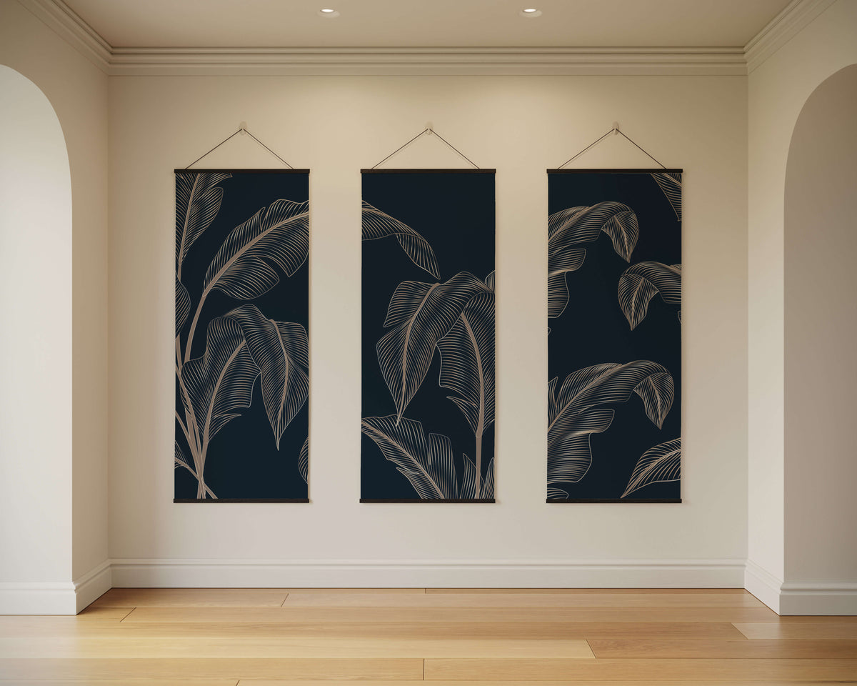 Three vertical navy blue banana leaf tapestries with white tropical line art hang on a light wall for decoration