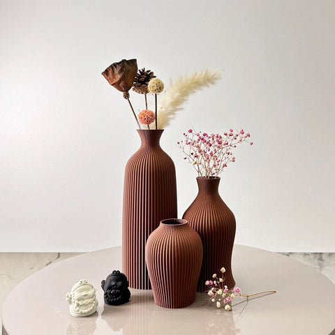 Three terracotta bara vases with vertical ribbed texture holding dried floral arrangements
