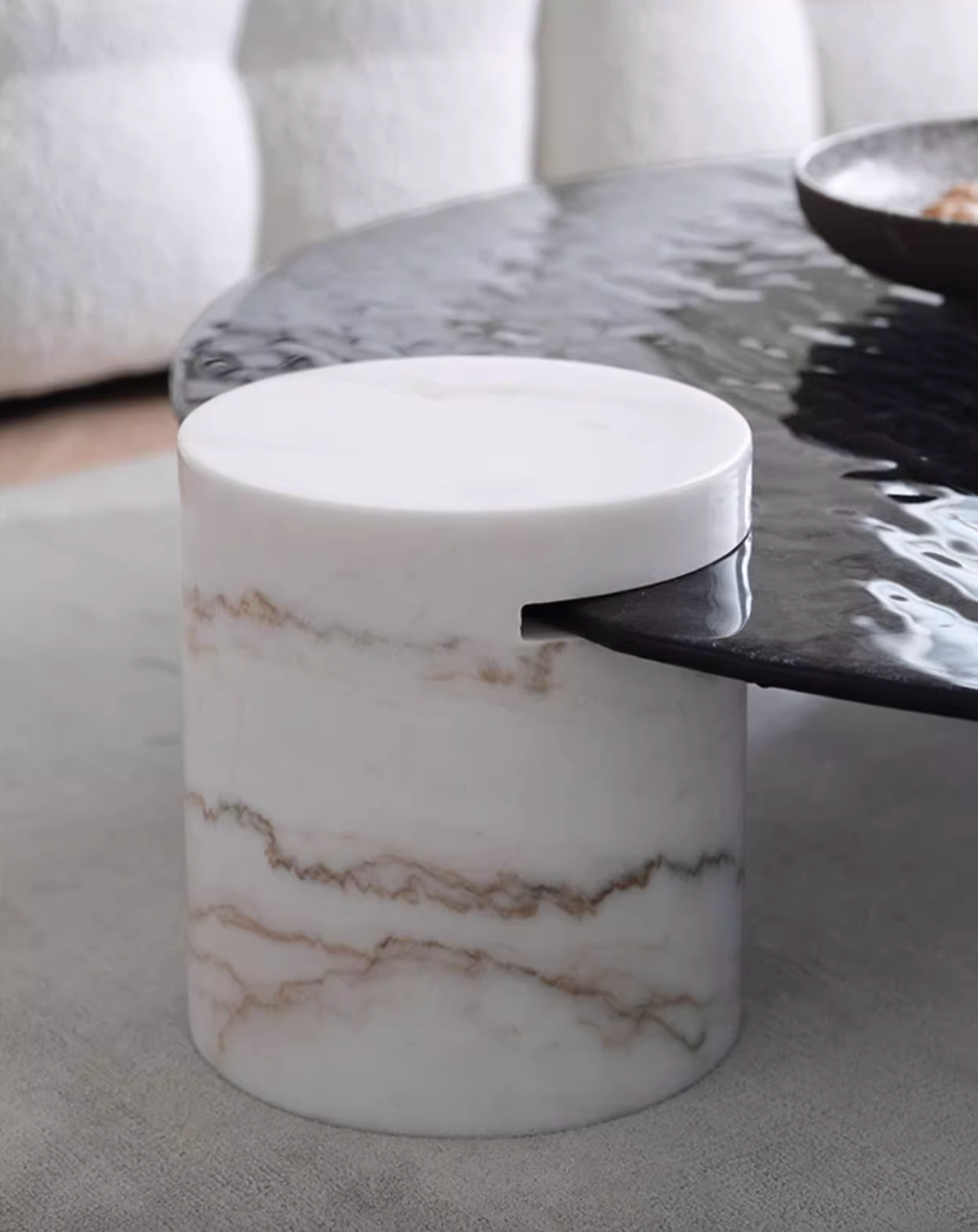 A sleek cylindrical white marble baxter coffee table with brown veining and a wave top finish
