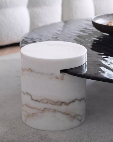 A sleek cylindrical white marble baxter coffee table with brown veining and a wave top finish