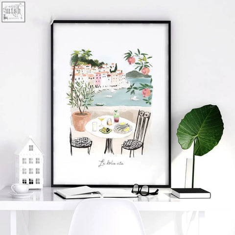 Watercolor wall art in black frame showing coastal scene with pink buildings dining table olive trees perfect beach art for dining room