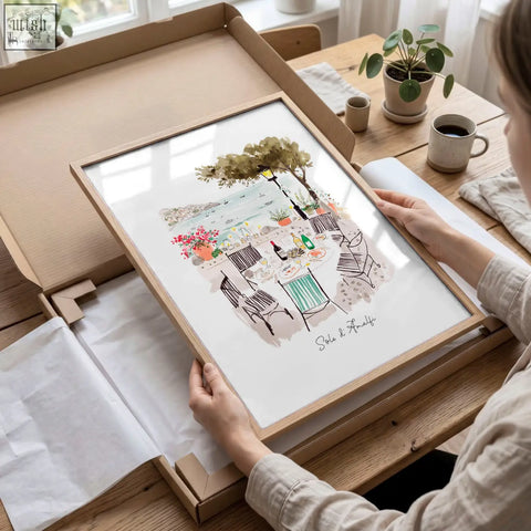 A framed watercolor beach artwork showing amalfi coast coastal dining scene under a tree in a light wood frame solo di amalfi