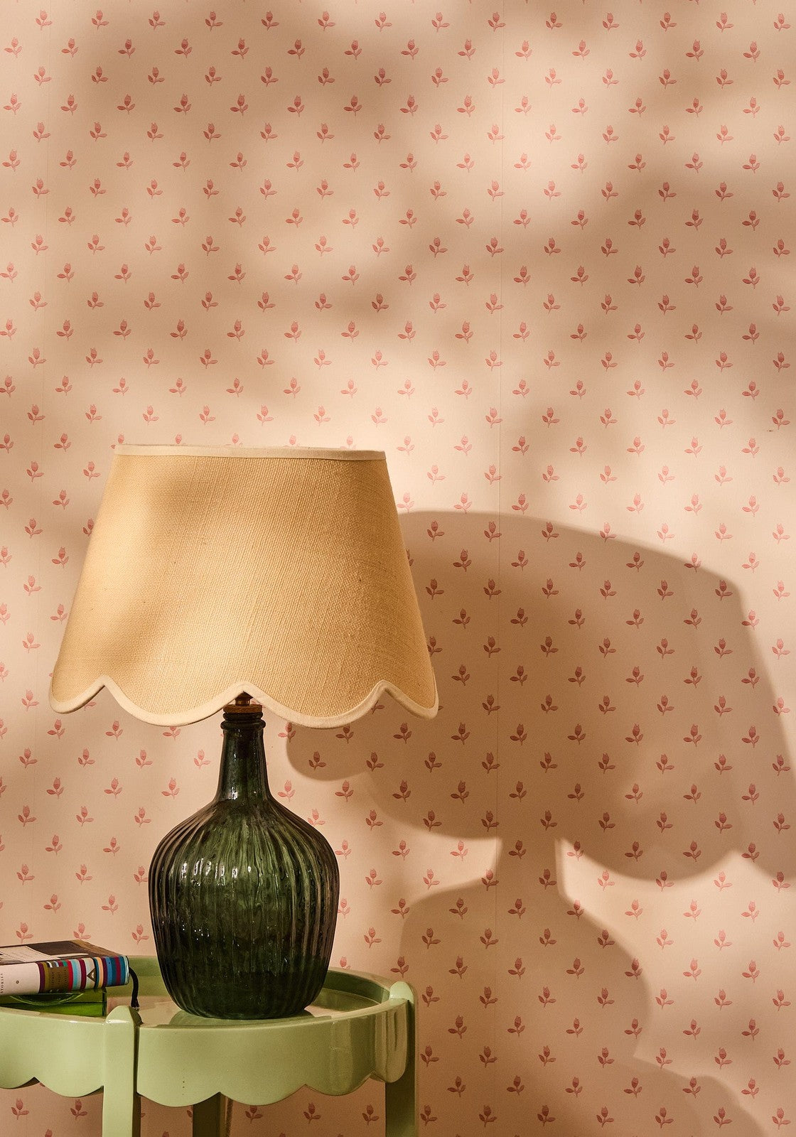 A dark green ribbed glass lamp with a beige scalloped fabric shade sits on a light green side table