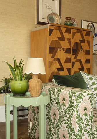 Mint green scalloped side table with woven wicker lamp and glossy green ceramic pot holding snake plant