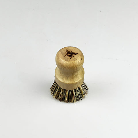 A light brown bamboo pot brush with natural bristles and a carved spider design on the handle for scrubbing pots