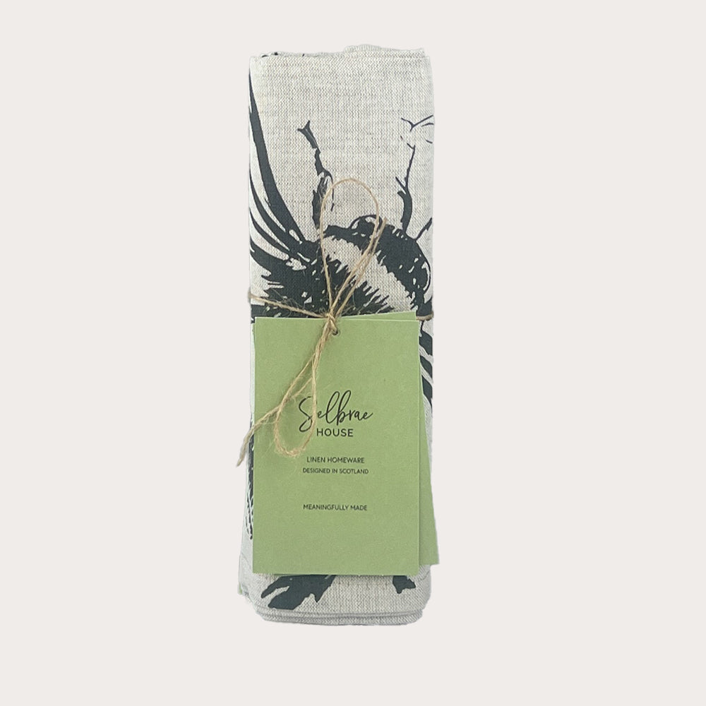 A rolled linen table runner with a black and white bird design tied with twine labeled selbrae house
