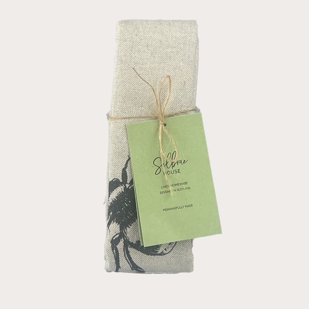 A light gray linen tea towel with a black embroidered bee design tied neatly from silfroe house