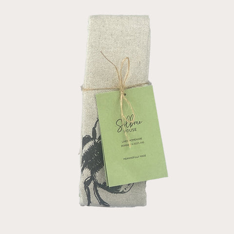 A light gray linen tea towel with a black embroidered bee design tied neatly from silfroe house