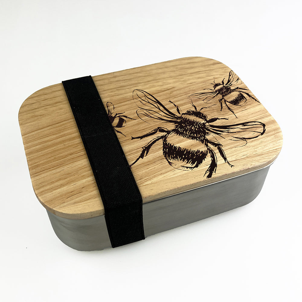 Rectangular wooden lunch box with engraved bee design and black fabric strap for easy carrying