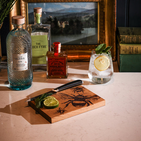 Wooden oak bar board with engraved bee design and black handle knife resting on the oak bar cutting board