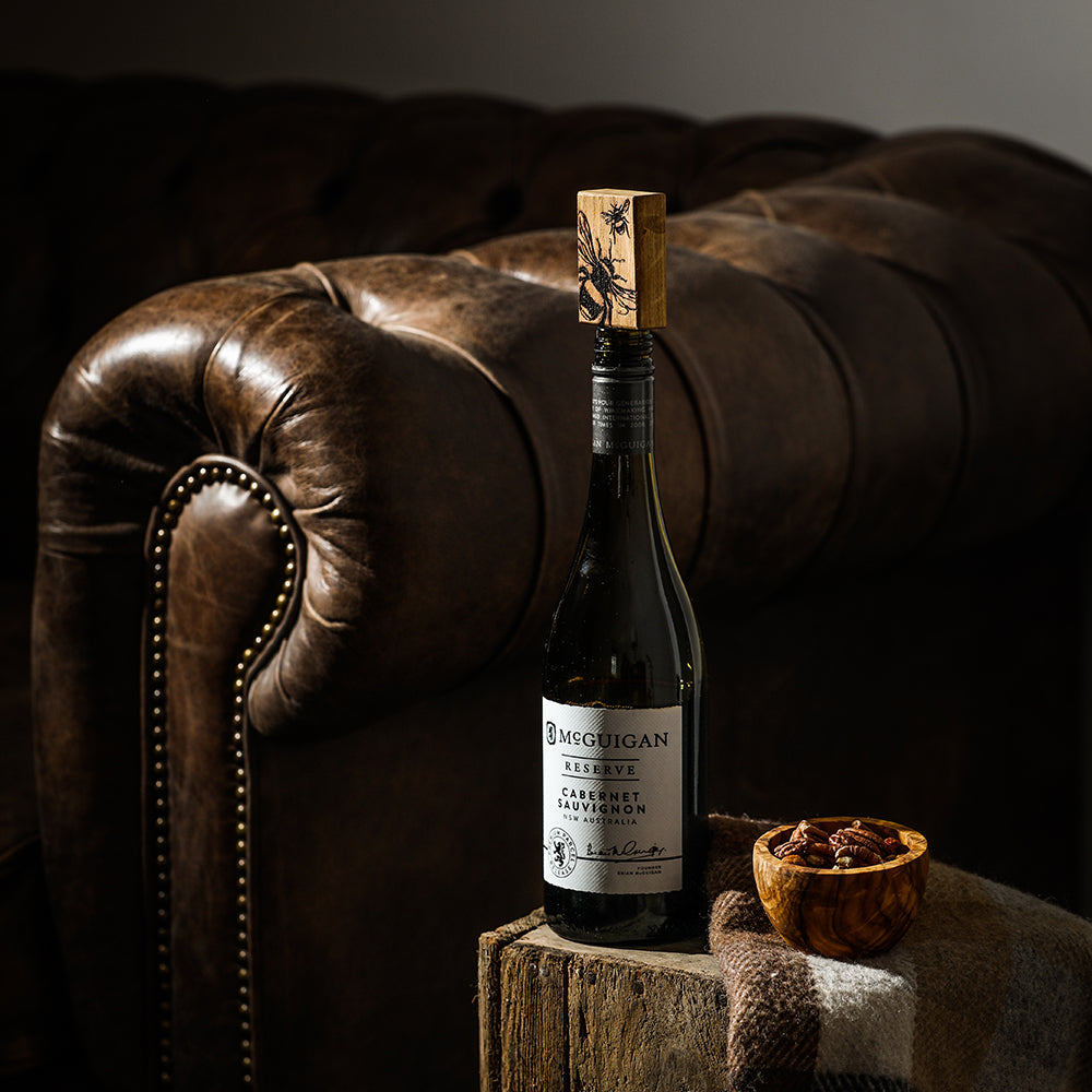 A dark glass mcguigan reserve cabernet sauvignon wine bottle with an engraved bee oak bottle stopper