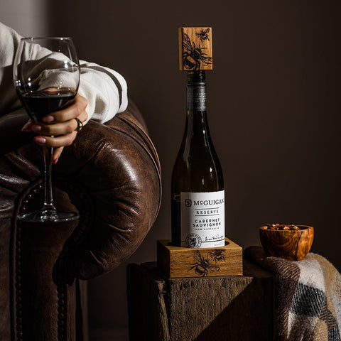 A dark green mcguigan reserve cabernet sauvignon bottle sealed with a bee engraved wooden stopper on an oak wine bottle coaster