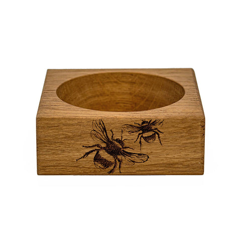 A light brown oak wine bottle coaster made of wood with a square shape and engraved bees on the side