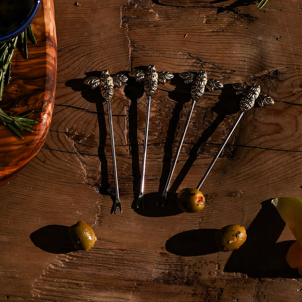 Set of four silver-toned bee olive picks with intricate detailing and slender metal shafts in a gift box