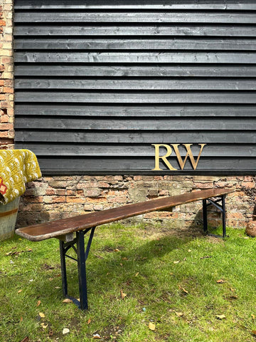 A long dark brown wooden folding beer festival bench with black metal legs against a brick and timber wall