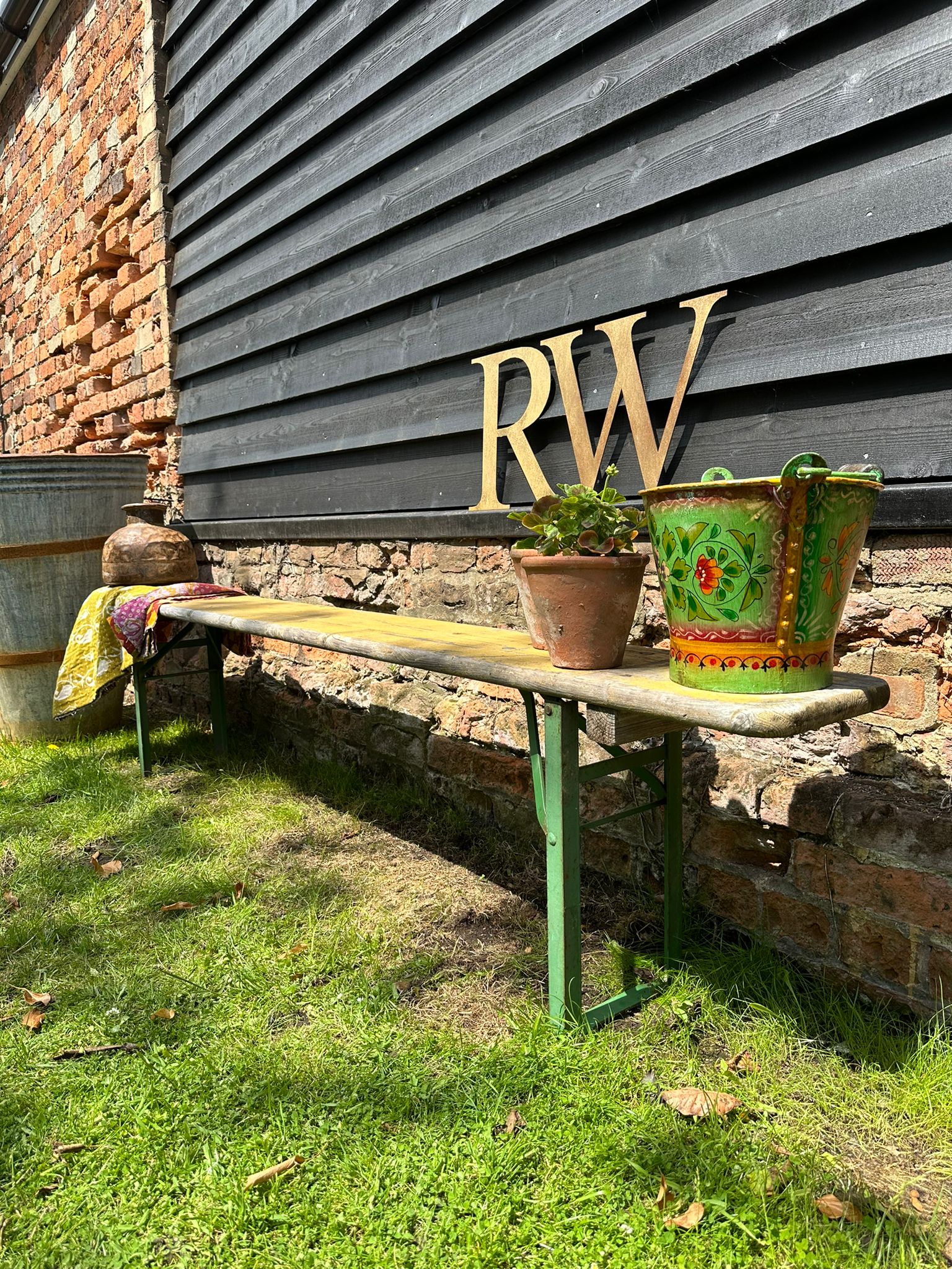 Green metal beer festival fold up bench with weathered wooden top against dark gray siding wall