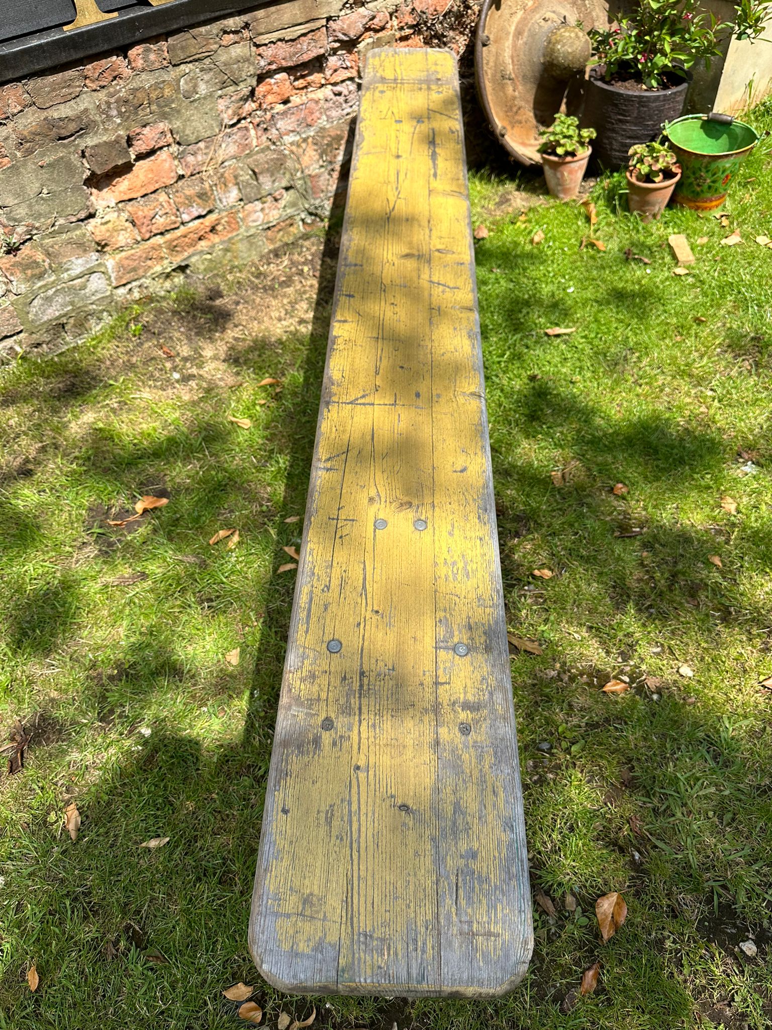 A weathered yellow wooden beer festival fold up bench with chipped paint sitting outdoors on grass