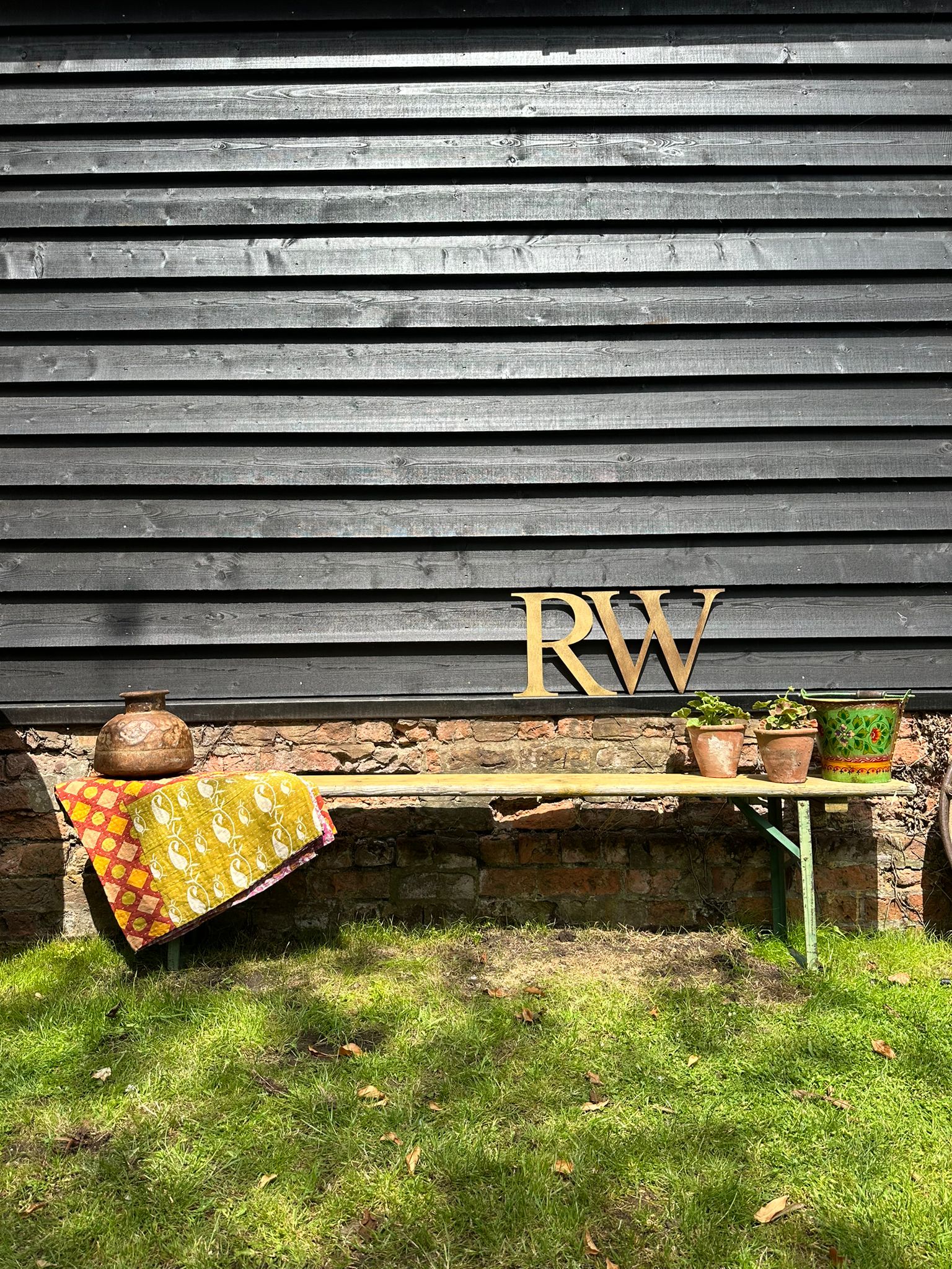 Gold-colored wooden rw monogram letters on dark gray wooden wall paired with beer festival fold up picnic bench