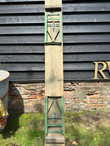 A rustic wooden beer festival fold up bench with green metal hinges and silver latch against dark wood paneling