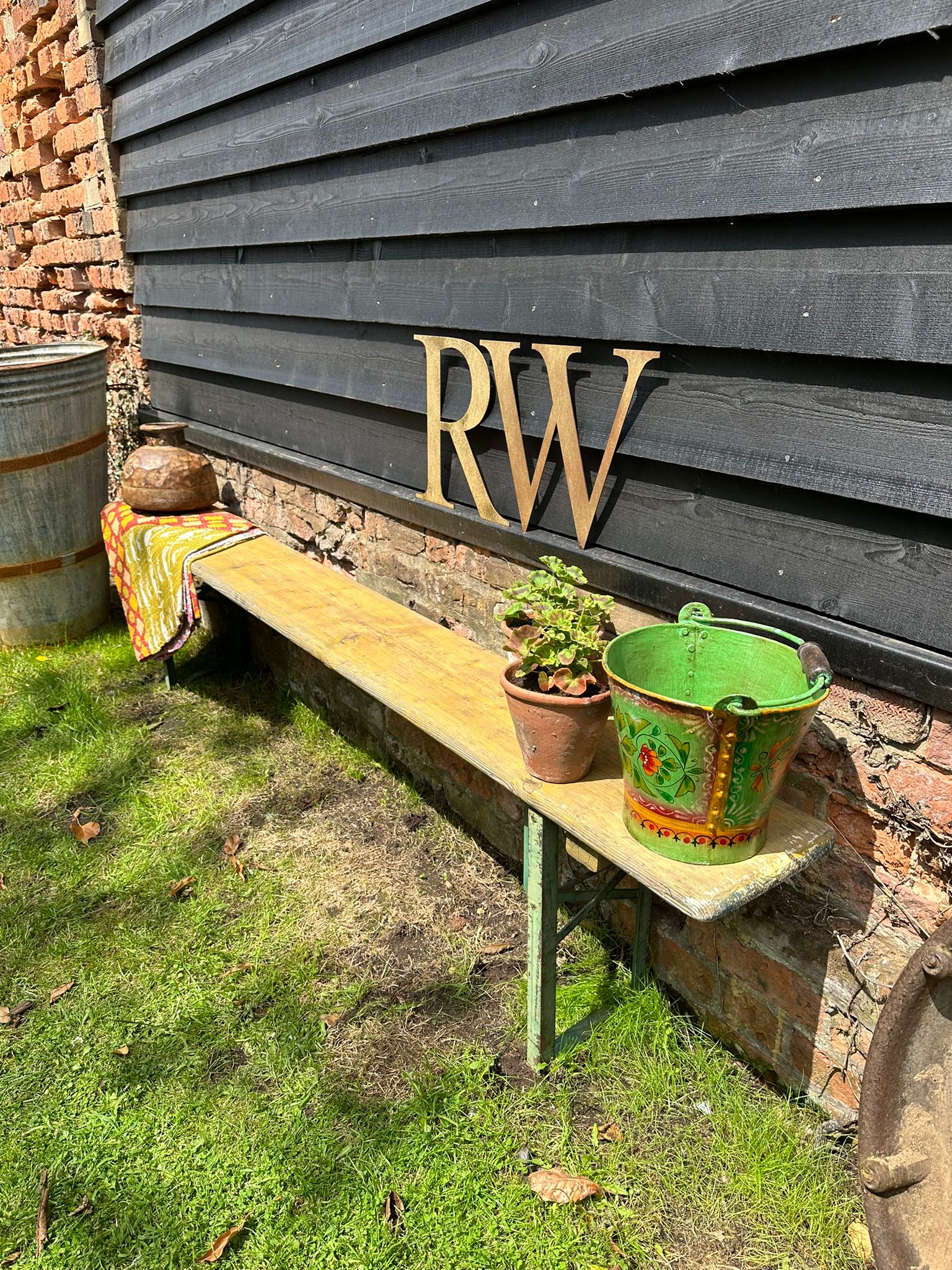 A rustic beer festival fold up bench with weathered yellow wooden seat and green metal legs against gray wall