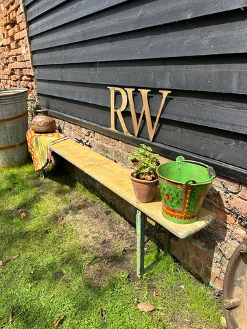 A rustic beer festival fold up bench with weathered yellow wooden seat and green metal legs against gray wall