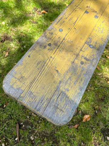 Weathered wooden beer festival fold up bench with peeling yellow paint and dark metal bolts for garden or hallway seating