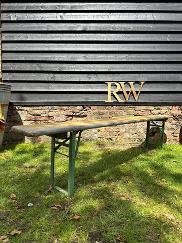 Green metal-framed beer festival fold up bench with weathered wooden seat for picnic or garden seating