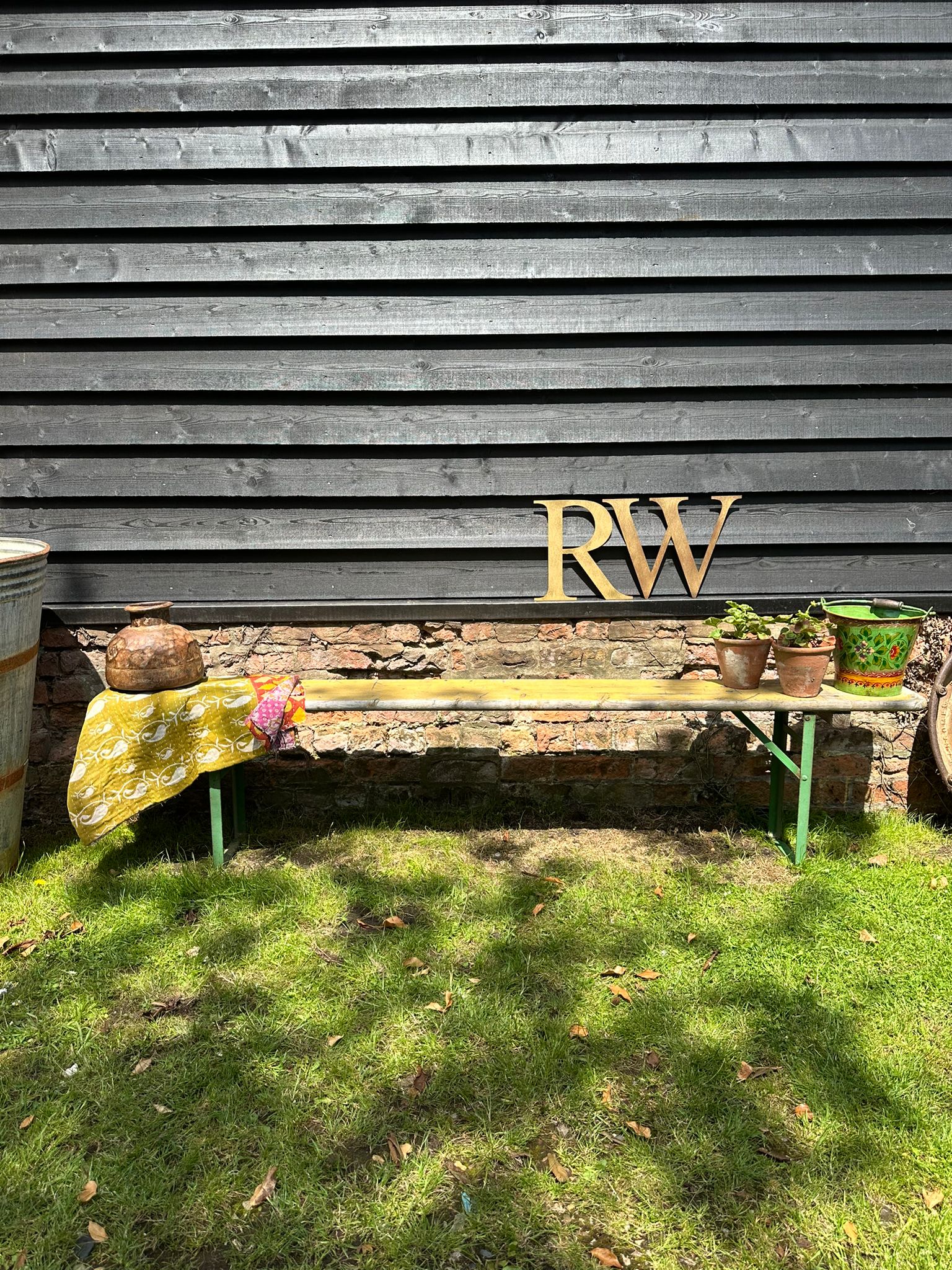 A rustic wooden beer festival fold up bench with green metal legs against a dark gray siding wall