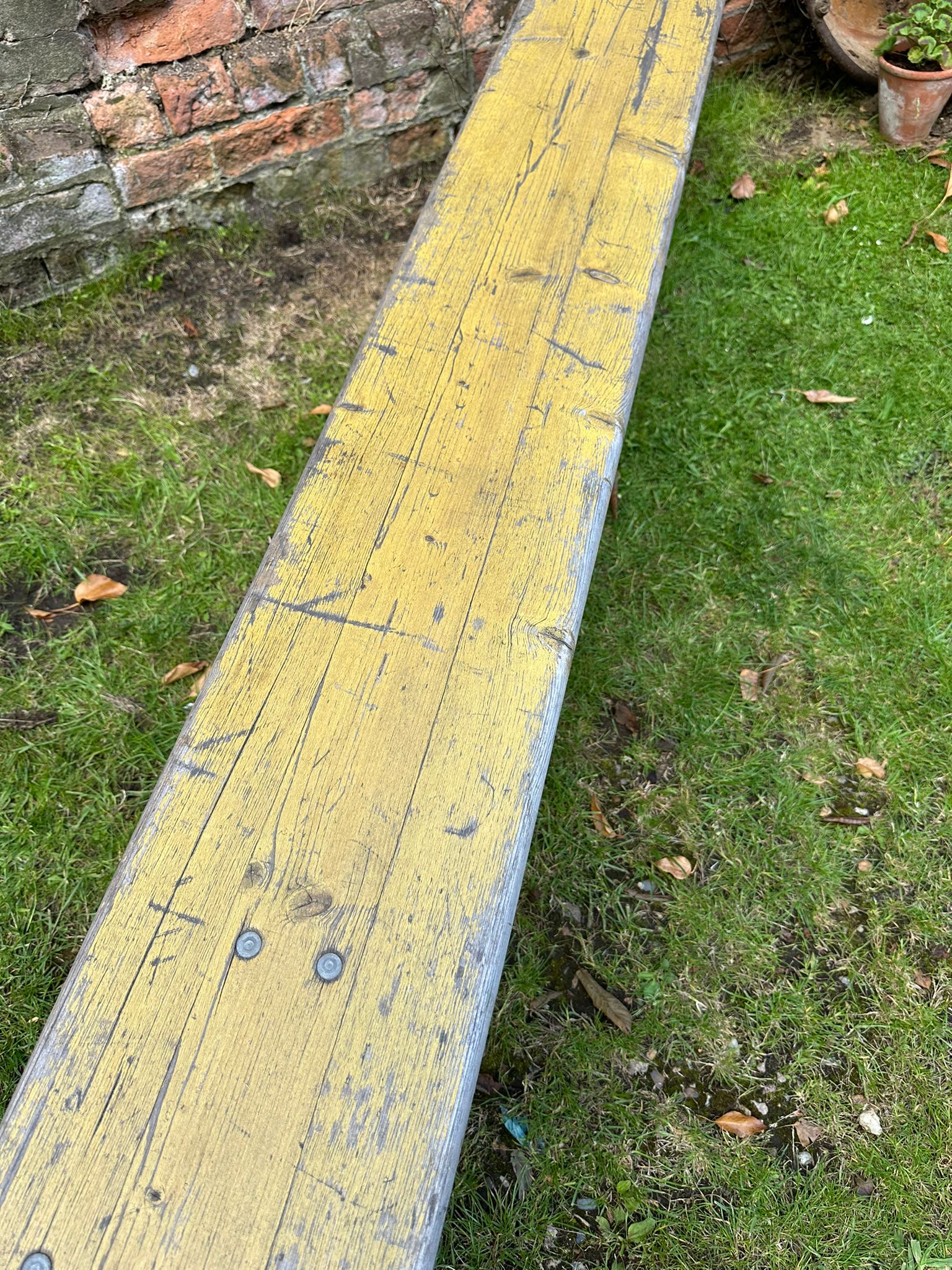 Weathered yellow wooden beer festival fold up bench with visible grain and nail heads for garden seating