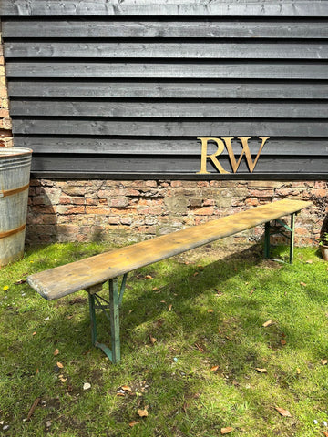 Long wooden beer festival fold up bench with green metal legs and weathered light brown surface for garden seating