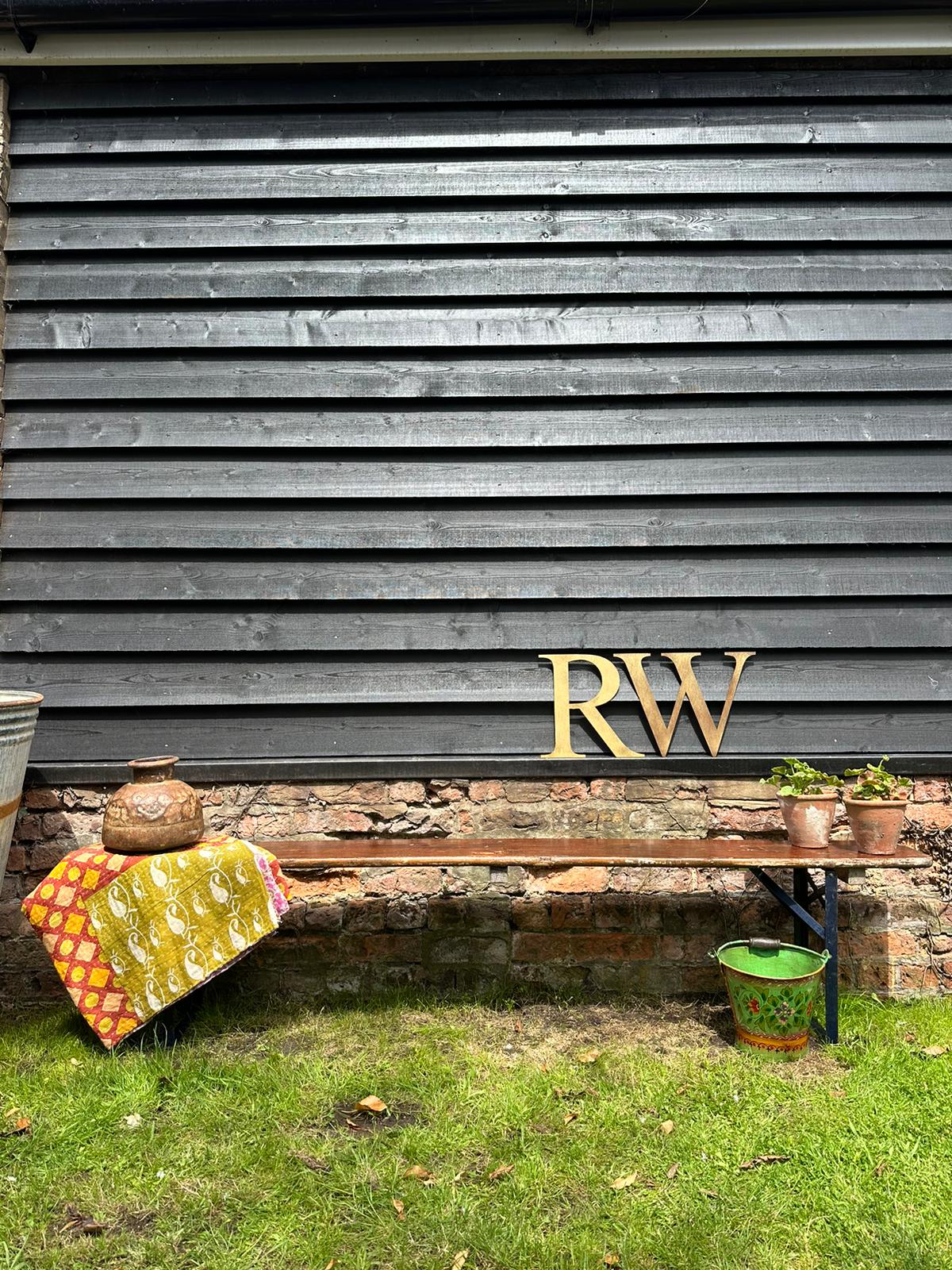 Gold metallic rw monogram on dark gray wood wall behind beer festival fold up bench for garden seating use