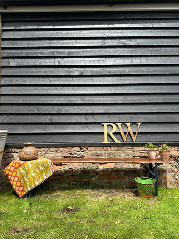 Gold metallic rw monogram on dark gray wood wall behind beer festival fold up bench for garden seating use